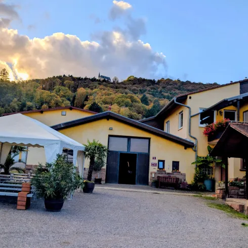 Ein einladendes Gebäude in ländlicher Umgebung mit einem Gartenbereich und einem Zelt. Die Landschaft im Hintergrund zeigt Hügel und einen schönen Himmel.