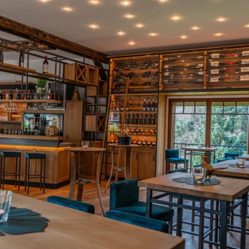 Ein gemütliches Restaurant mit Holzregalen, die eine Auswahl an Getränken zeigen. Die Einrichtung ist modern und einladend, mit Barhockern und Tischen.