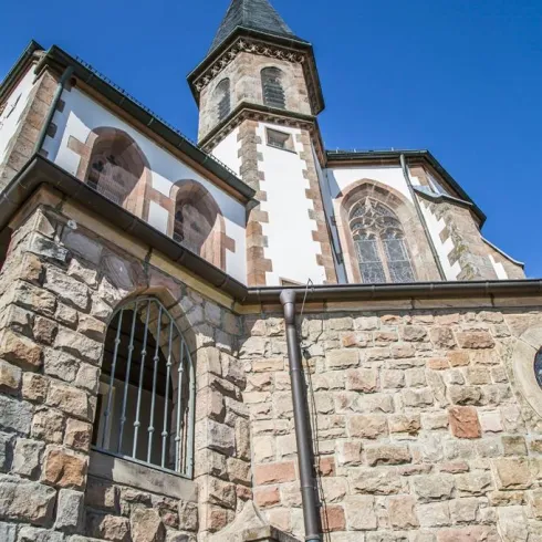 Eine historische Kirche mit einer markanten Spitze und schönen Steinmauern. Der Himmel ist klar und blau im Hintergrund.
