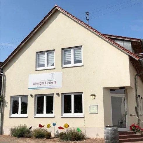 Ein Weingut mit einem hellen Gebäude und einer einladenden Fassade. Bunte Pflanzenornamente schmücken den Eingangsbereich.