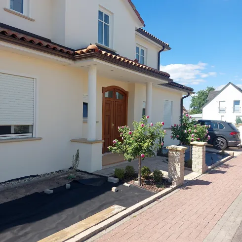 Ein modernes Haus mit einem liebevoll gestalteten Eingang. Im Vordergrund sind Pflanzen und ein gepflasterter Weg zu sehen.