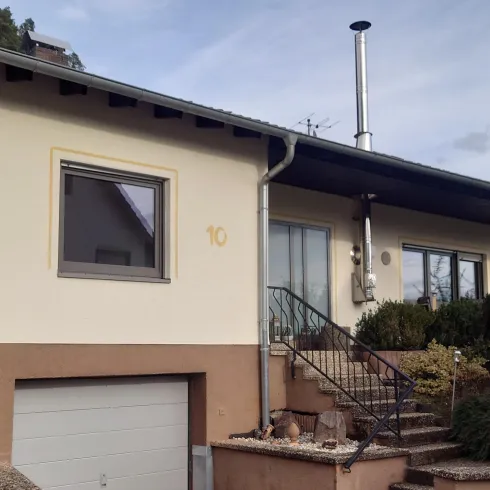 Ein modernes Einfamilienhaus mit hellem Außenanstrich und einem kleinen Garten. Die Treppe führt zur Eingangstür, und es gibt eine Garage auf der linken Seite.
