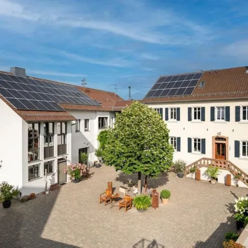 Ein modernes Gebäudeensemble mit Solarpanels und einem begrünten Innenhof. Die Architektur verbindet traditionelles Design mit nachhaltiger Technologie.