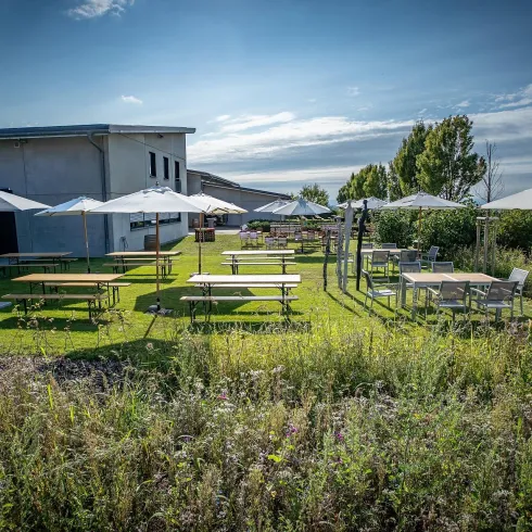 Ein schöner Außenbereich mit Tischen und Sonnenschirmen. Die Umgebung ist grün und lädt zum Verweilen ein.