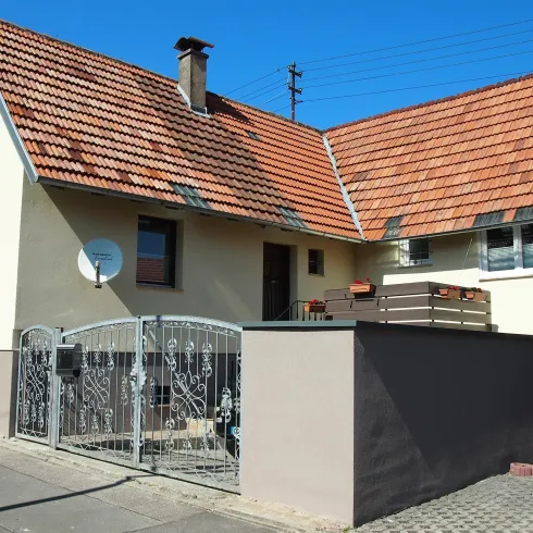 Ein einladendes Wohnhaus mit einem roten Ziegeldach. Der Eingangsbereich ist von einem modernen Zaun umgeben.