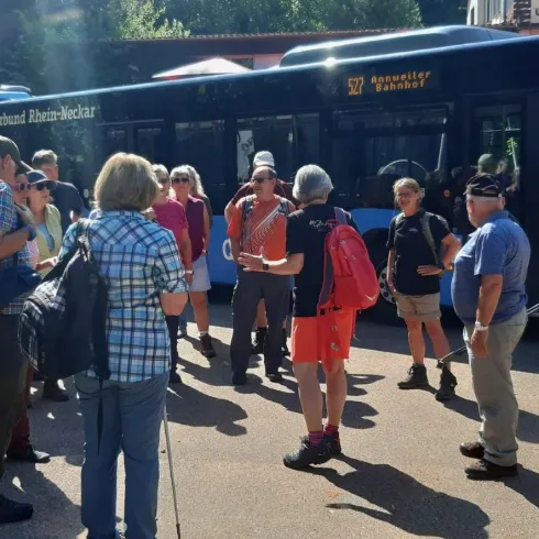 Eine Gruppe von Menschen steht vor einem blauen Bus. Sie scheinen auf den Einstieg in den Bus zu warten.