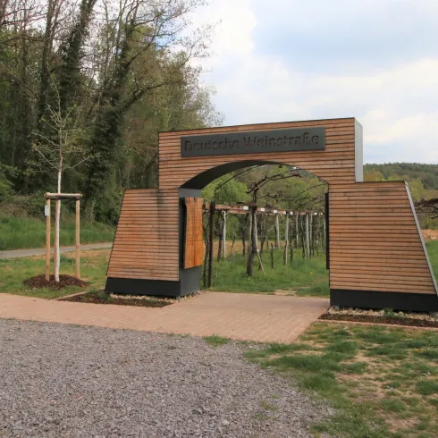 Ein Eingang zu einem Weinberg, umgeben von Bäumen und Wiesen. Die Struktur ist modern und einladend gestaltet.