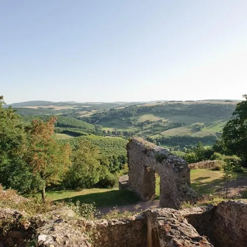 Eine malerische Landschaft mit sanften Hügeln und üppigem Grün. Im Vordergrund sind die Ruinen einer alten Mauer zu sehen.