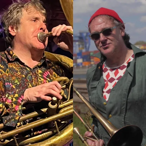 Ein Musiker singt und spielt Gitarre, während eine Cellistin neben ihm spielt. Hintergrundlich sind bunte Lichter zu sehen, die eine lebendige Atmosphäre schaffen.