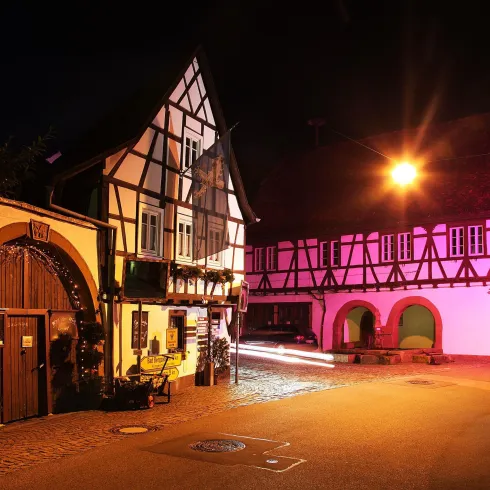 Eine malerische Straßenansicht bei Nacht mit historischen Fachwerkhäusern. Die Gebäude sind sanft beleuchtet, was eine gemütliche Atmosphäre schafft.