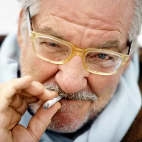 Ein Musiker singt und spielt Gitarre, während eine Cellistin neben ihm spielt. Hintergrundlich sind bunte Lichter zu sehen, die eine lebendige Atmosphäre schaffen.