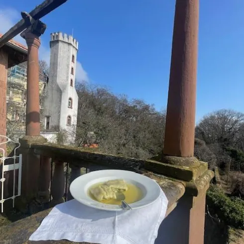 Ein Teller mit Suppe steht auf einem Tisch im Freien. Im Hintergrund ist ein historischer Turm und ein blauer Himmel zu sehen.