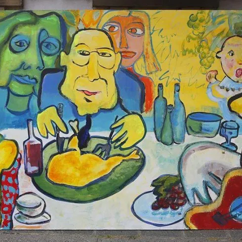 Ein lebendiges Wandbild mit bunten Figuren, die an einem Tisch sitzen und Essen genießen. Die Darstellung zeigt eine fröhliche Atmosphäre mit Getränken und einer Gitarre.