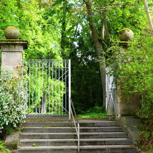 Ein schöner Eingang mit einem Gittertor und Steinpfeilern. Umgeben von üppigem Grün und Blumen.
