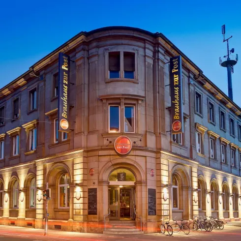 Ein historisches Gebäude mit einer einladenden Fassade und sanfter Beleuchtung. Es gibt Fahrräder vor dem Eingang und Werbeschilder für ein Restaurant.