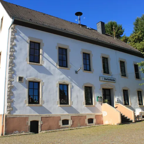 Ein großes, historisches Gebäude mit weißen Wänden und vielen Fenstern. Es liegt in einer grünen Umgebung und hat eine einladende Atmosphäre.