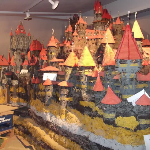 Eine detaillierte Modellstadt mit hohen Burgen und roten Dächern ist zu sehen. Die Landschaft ist künstlich gestaltet und zeigt verschiedene Höhenlagen.