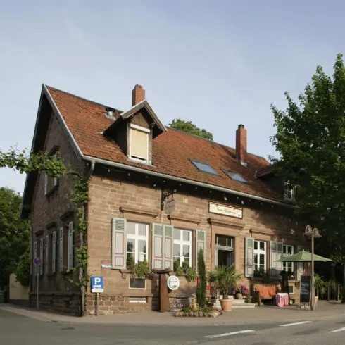 Ein charmantes Gebäude mit einer roten Dachkonstruktion und grünen Fensterläden. Es ist von Bäumen umgeben und hat ein gemütliches Ambiente.