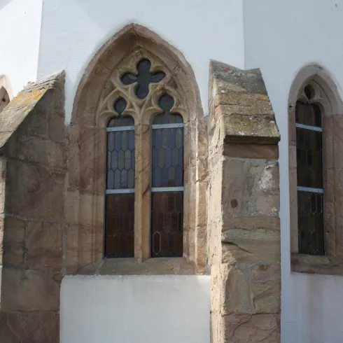 Ein historisches Gebäude mit einer weißen Fassade und gotischen Fenstern. Die Architektur hat markante Steinelemente und lässt auf eine lange Geschichte schließen.