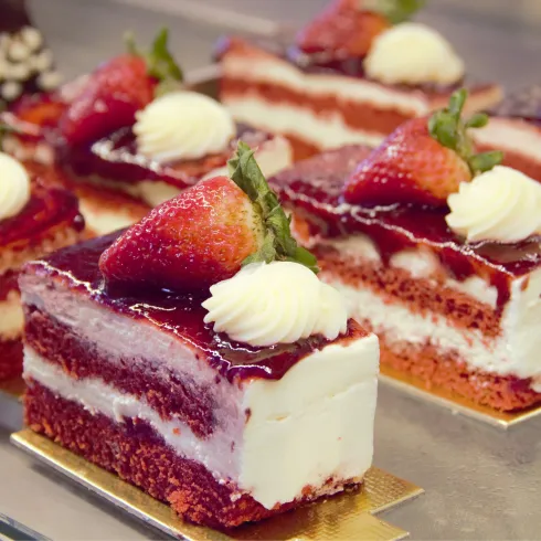 Eine köstliche Torte mit Schichten aus Biskuit, Sahne und Erdbeeren. Oben ist sie mit roter Fruchtsauce und Sahne verziert.