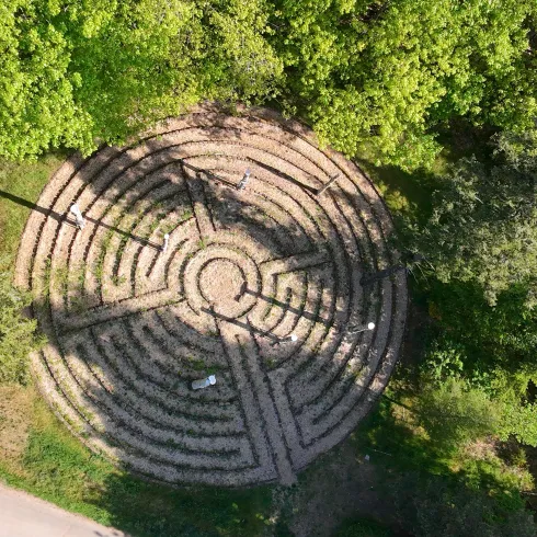 Ein runder Gartenlabyrinth aus Steinen, umgeben von Bäumen. Der Weg im Labyrinth ist gut erkennbar und führt zum Zentrum.