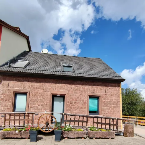 Ein hübsches Haus mit einem dunklen Dach und bunten Fenstern. Im Vordergrund befindet sich ein Holzgeländer mit Blumen.