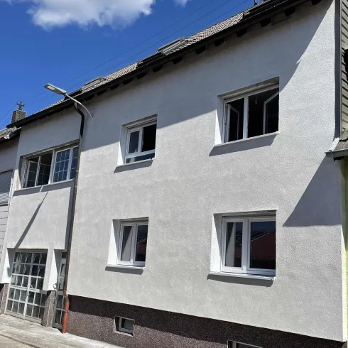 Ein modernes Wohnhaus mit weißen Wänden und mehreren Fenstern. Die Fassade ist schlicht und gut erhalten.