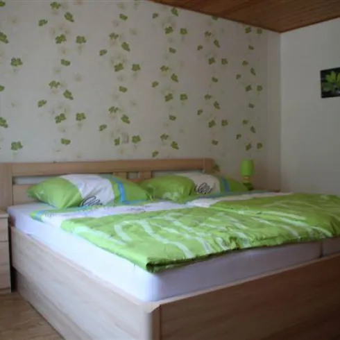 Ein gemütliches Schlafzimmer mit einem Doppelbett und frischer grüner Bettwäsche. Die Wände sind mit Blumenmustern dekoriert, und es gibt zwei Nachttische mit grünen Lampen.