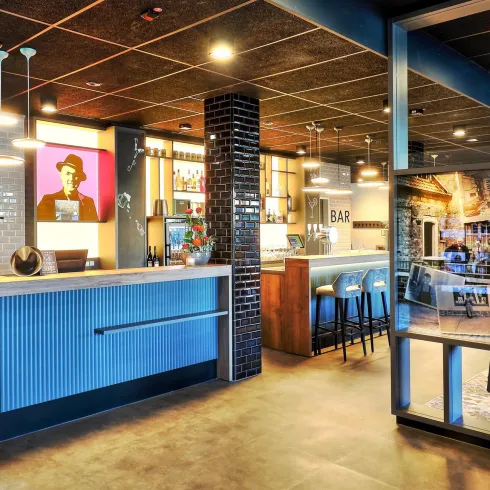 Eine moderne Bar mit Holz- und Metallakzenten. Helle Beleuchtung und eine einladende Atmosphäre prägen den Raum.