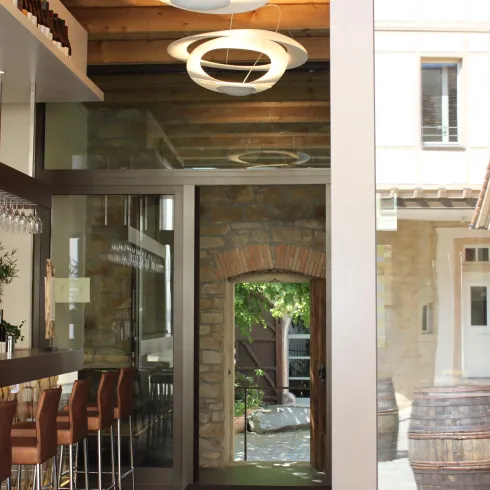 Ein modernes Café mit Holz- und Glaselementen. Im Hintergrund sind alkoholische Fässer und ein gewölbter Eingang sichtbar.