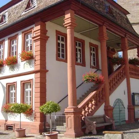 Das alte Rathaus und somit auch der Standort des I -Punkts. Das Gebäude ist umgeben von einer Kirche und gepflastertem Boden. Das Gebäude ist rot weiß.