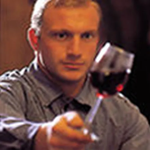 Ein Winzer mit einem Glass Wein in der Hand, im Hintergrund Weinfässer, von Weingut Kreuzhof.