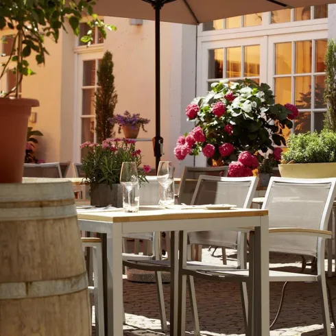 Ein gemütlicher Außenbereich mit einem Tisch, Stühlen und einem Sonnenschirm. Blumen und Pflanzen sorgen für eine einladende Atmosphäre.