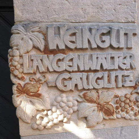 Ein in Steingemeiselter Schriftzug, auf dem " Weingut Langenwalter- Gauglitz " geschrieben steht.