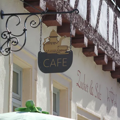 Ein mit Holzbalken versehenes, weißes Gebäude an dem ein Schild außen hängt, auf dem "Cafe" geschrieben steht.