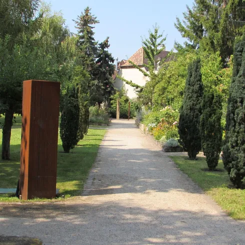 Ein Kiesweg im Apothekergarten. Dieser Weg mit Zypressen und einer Skulptur, die an beiden Seiten den Weg verschönern.