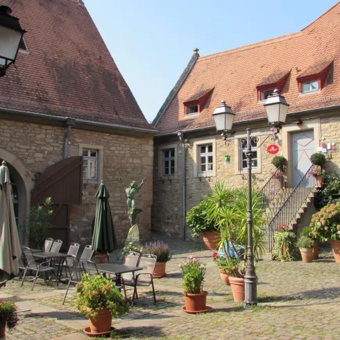 Ein malerischer Innenhof mit Steinen und Pflanzen. Rund um den Hof befinden sich Sitzgelegenheiten und laternen.