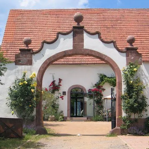 Ein hübsches Gebäude mit einem bogenförmigen Eingang und bunten Blumen. Der Himmel ist blau und die Umgebung ist grün und einladend.