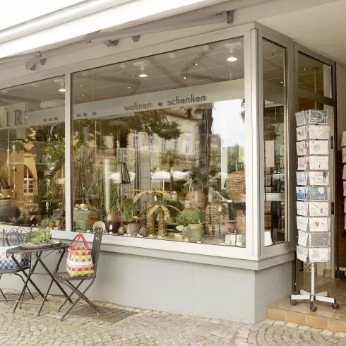 Ein einladendes Geschäft mit dem Namen "FLAIR". Draußen stehen ein Tisch und Stühle, und im Schaufenster sind verschiedene Dekorationsartikel zu sehen.