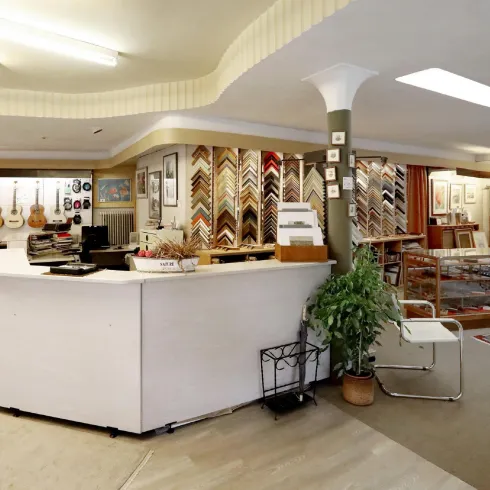 Ein helles Geschäft mit einem Empfangstresen und einem Bereich für Rahmen. An der Wand hängen Gitarren und Bilderrahmen in verschiedenen Stilen.