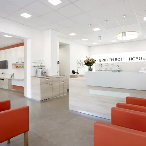 Ein moderner Empfangsbereich mit einem hellen, freundlichen Design. Rote Sessel und eine helle Theke prägen das Ambiente.