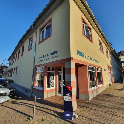 Ein Geschäftshaus an einer Ecke mit einem Schild für "schabale & muller". Es gibt einige Boote auf dem Parkplatz und eine klare blaue Himmel im Hintergrund.