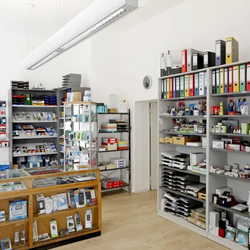 Ein gut sortierter Ladensraum mit Regalen voller Büromaterialien und Zubehör. Auf der Verkaufstheke befinden sich verschiedene Artikel und Stationery-Produkte.