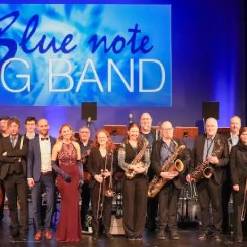 Eine Big Band steht auf der Bühne mit verschiedenen Instrumenten. Im Hintergrund leuchtet ein Banner mit dem Schriftzug "Blue Note BIG BAND".