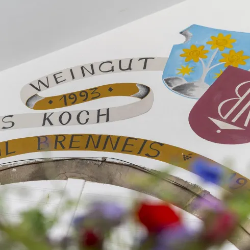 Ein Weingutsschild mit den Namen Matthias Koch und Emil Prenneis. Die Wappen und Blumen verleihen dem Bild einen traditionellen Charme.