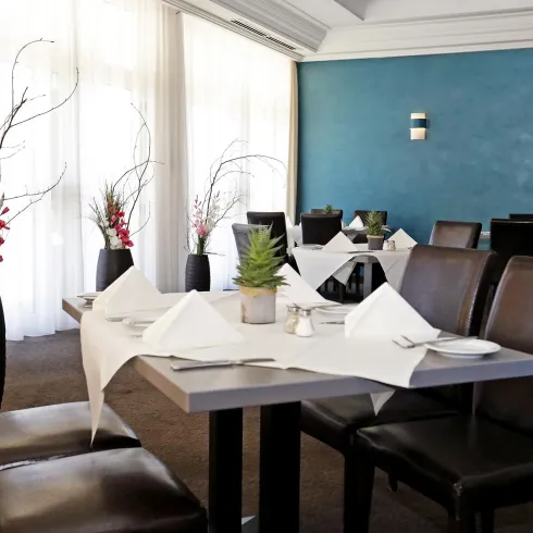 Ein elegantes Restaurant mit einem Tisch, der für Gäste gedeckt ist. Die Wände sind sanft blau gestrichen und es gibt ansprechende dekorative Elemente.