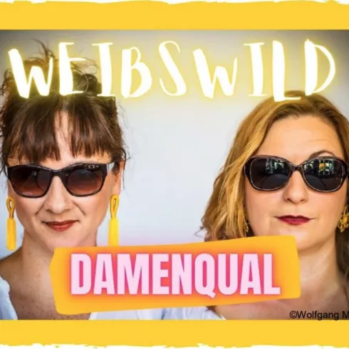 Zwei Frauen mit Sonnenbrillen posieren für ein Foto. Der Hintergrund zeigt den Schriftzug „WEIBSWILD“ und „DAMENQUAL“.