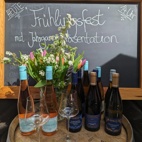 Ein Frühlingsfest mit einer Präsentation von Jahrgängen. Im Vordergrund stehen Weinflaschen und Gläser, umgeben von frischen Blumen.