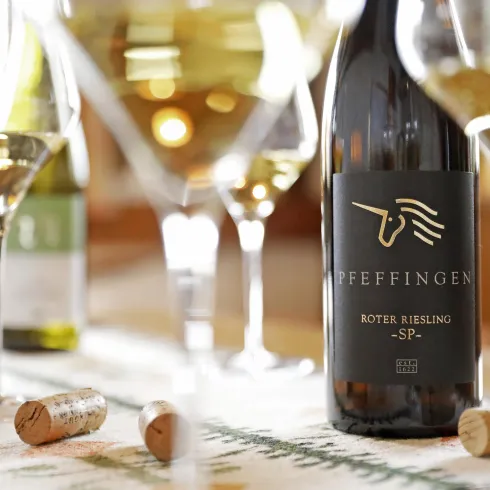 Eine elegante Präsentation von Weinen mit einem Fokus auf eine Flasche "Roter Riesling". Im Hintergrund sind mehrere Weingläser und Korken sichtbar.