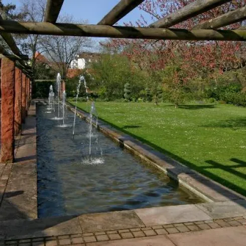 Ein schöner Garten mit einem Wasserlauf und dezenten Springbrunnen. Die Umgebung ist grün und einladend.